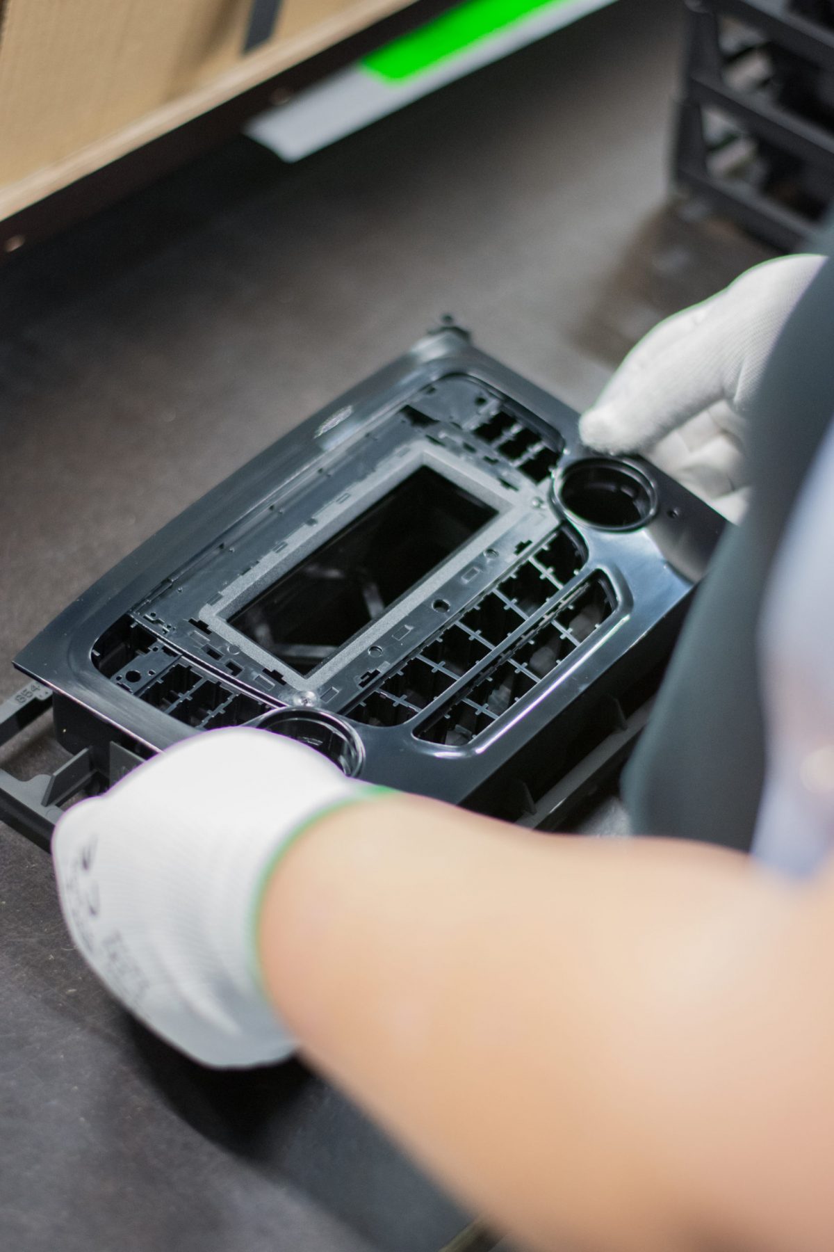 Twee handen (van een Bewel-medewerker) assembleren auto-onderdelen, meer bepaald een autoradio of een deel van een dashboard.