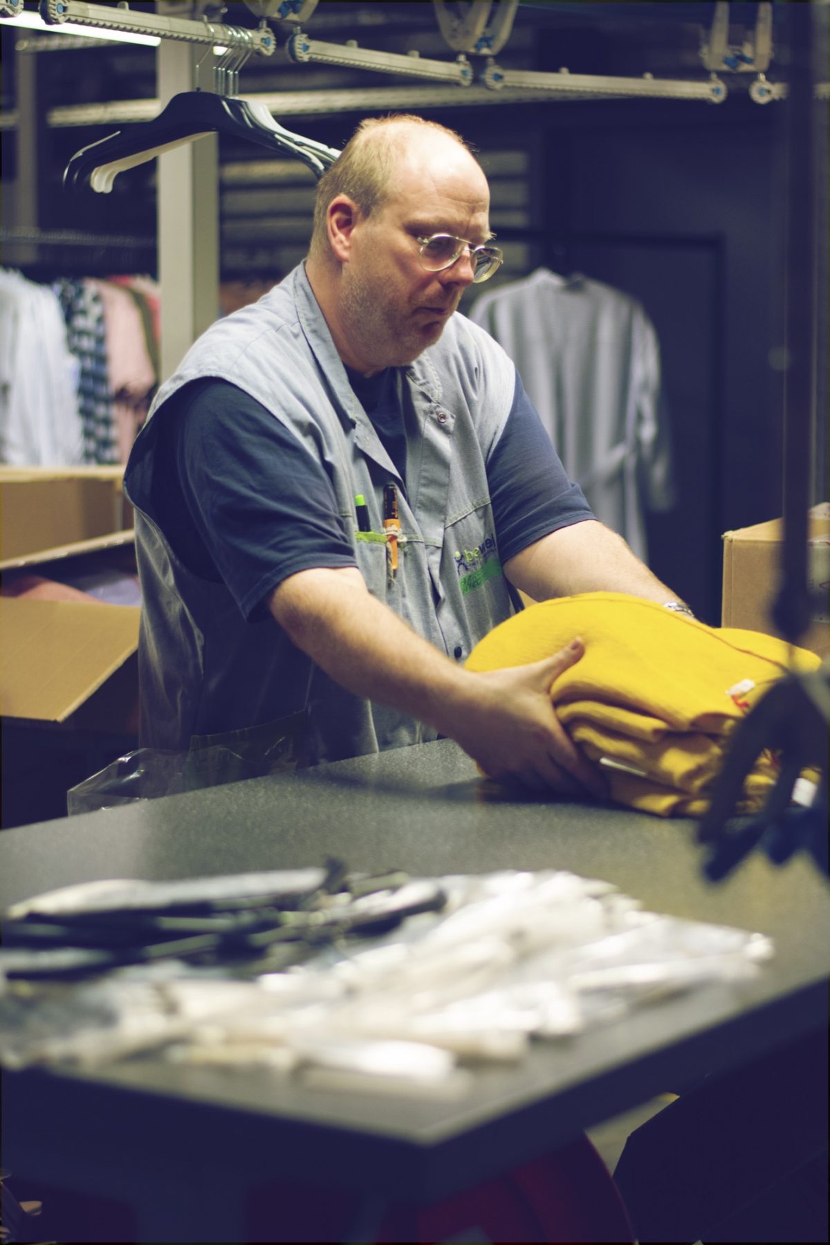 Een medewerker van Bewel controleert gele T-shirts aan een werktafel en plooit ze netjes op.