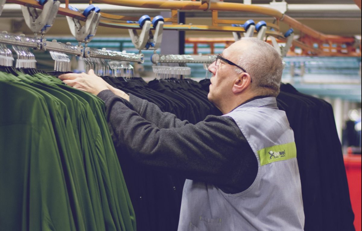 Een medewerker van Bewel doet aan textieconditionering voor kledingzaken zoals JBC en La Bottega. Hij controleert khaki hemden op de foto, die op kapstokken hangen.