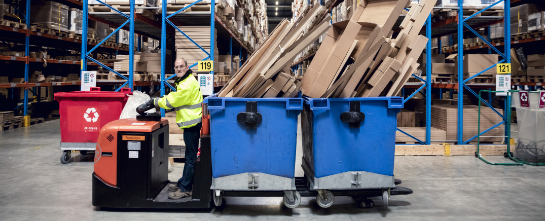 Een medewerker van Bewel rijdt rond in het magazijn van Ikea. Hij vervoert twee blauwe containers vol met grote kartonnen dozen.